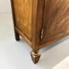 Close-up of a wooden cabinet leg with a turned, gold-accented foot and brass hardware, highlighting the wood grain.