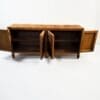 Wooden sideboard with two open doors showing interior shelves against a pale background.