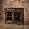 Antique dark wood cabinet with ornate metal grille doors against a brick wall.