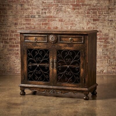 Antique dark wood cabinet with ornate metal grille doors against a brick wall.